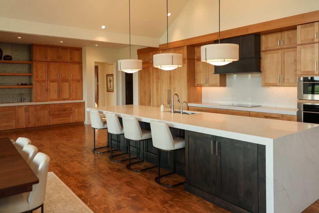 A spacious kitchen with hanging lights, a marble counter, and white stool chairs.