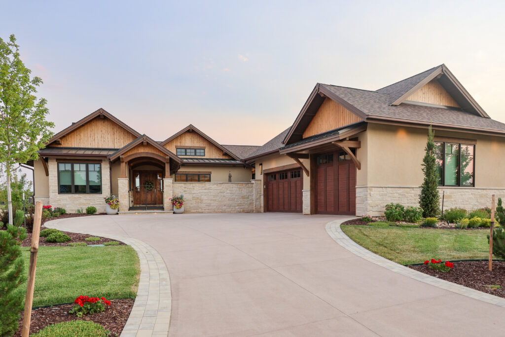 The outside of a beautiful house with wooden garage doors, a wide driveway and green lawn.