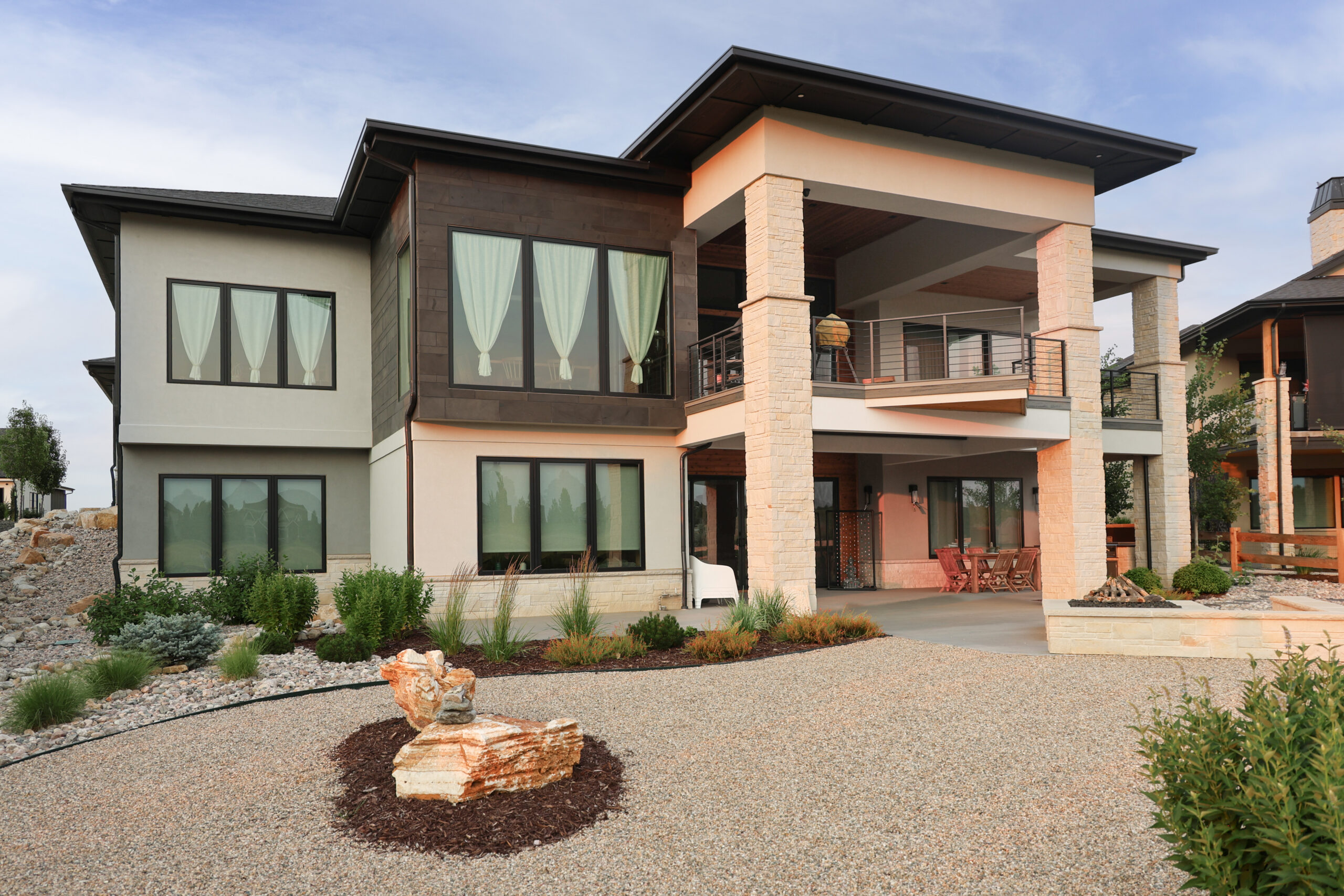 The outside of a house at sunset with large windows and a two story patio.
