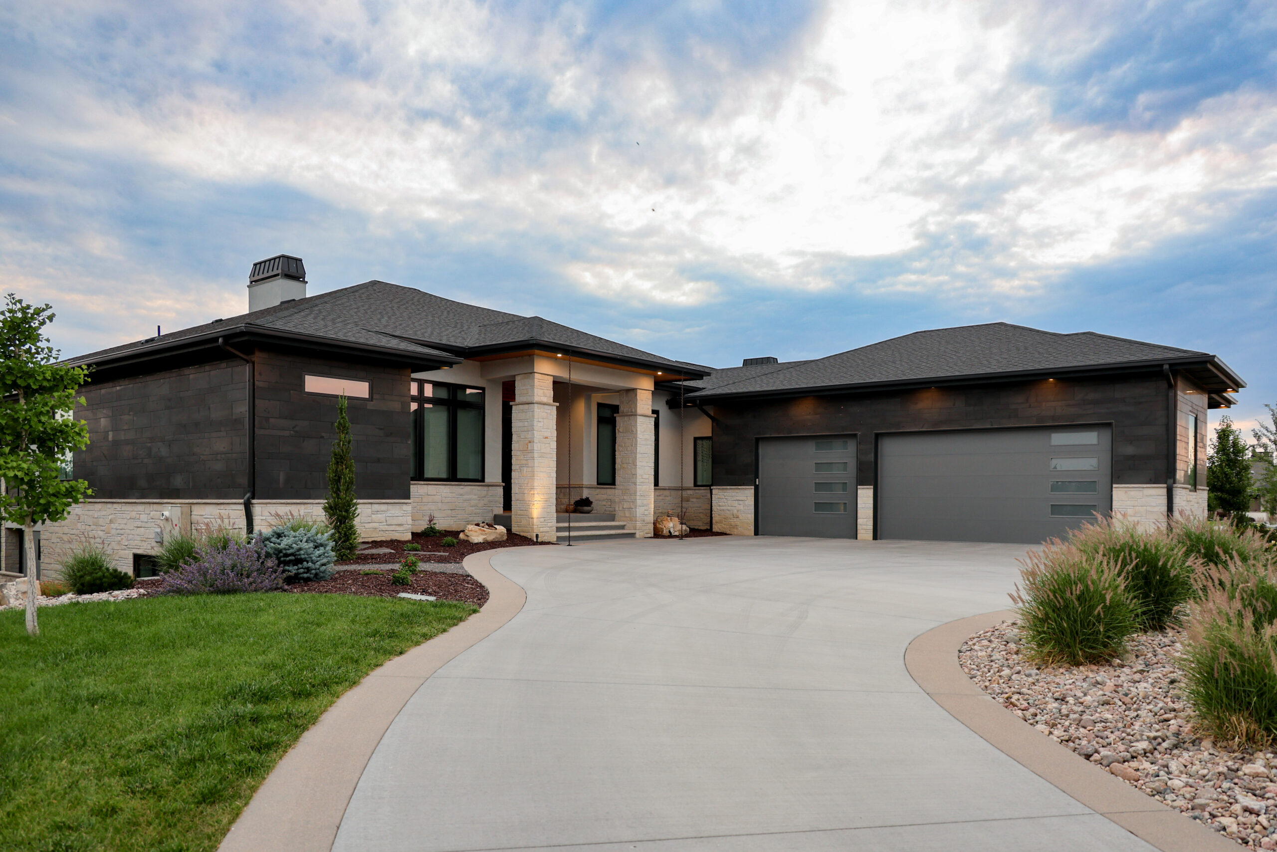 The outside of a house with gray garage doors and stone pillars in front of the door.