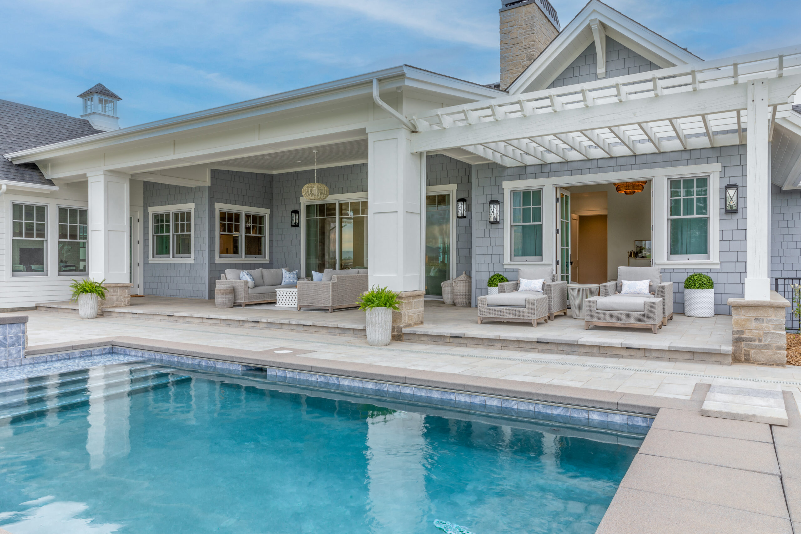 The outside of a beautiful blue and white house with a a pool in the backyard and patio furniture