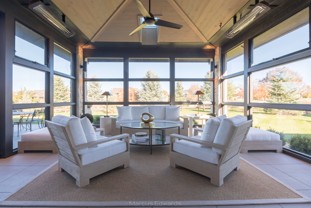 A large sun room with floor to ceiling windows on all sides and large white stuffed chairs around a coffee table.