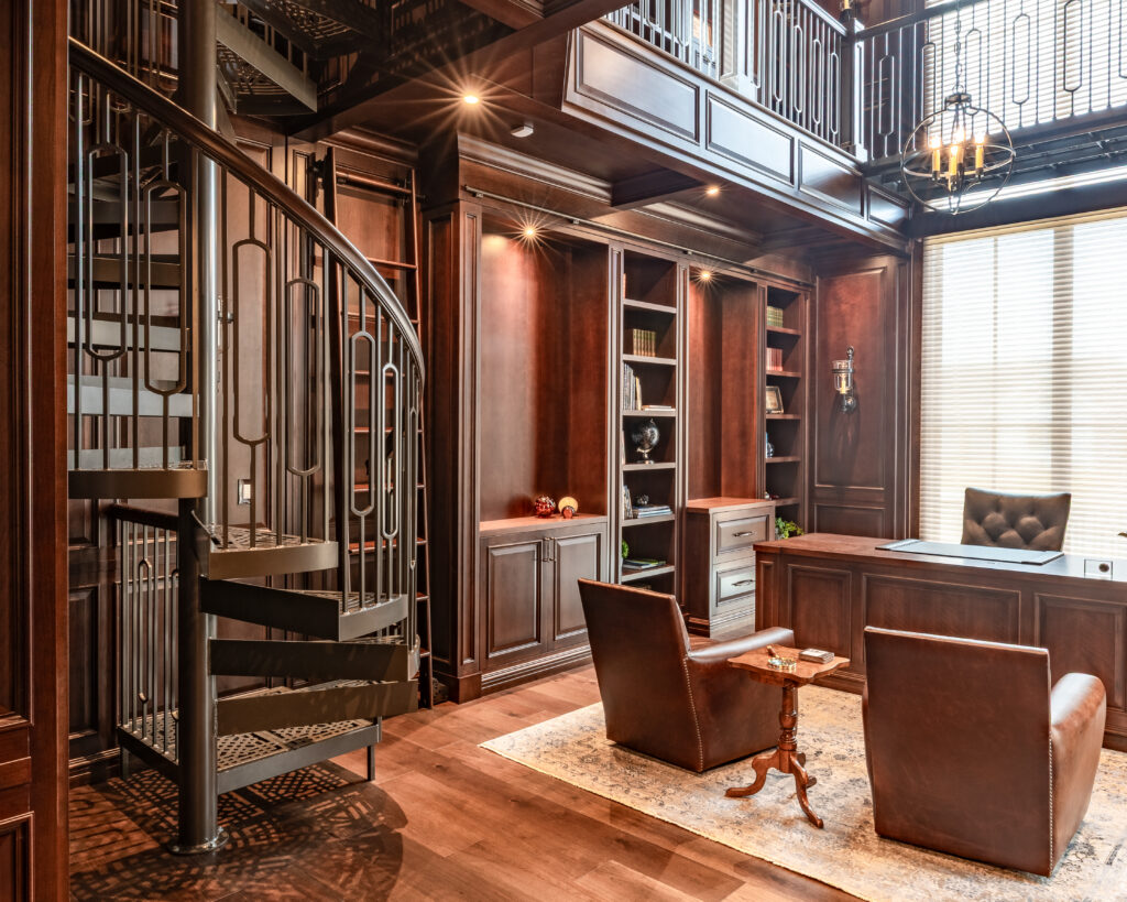 Dark paneled wood office and library space with a large wooden desk and leather chairs with a metal spiral staircase.