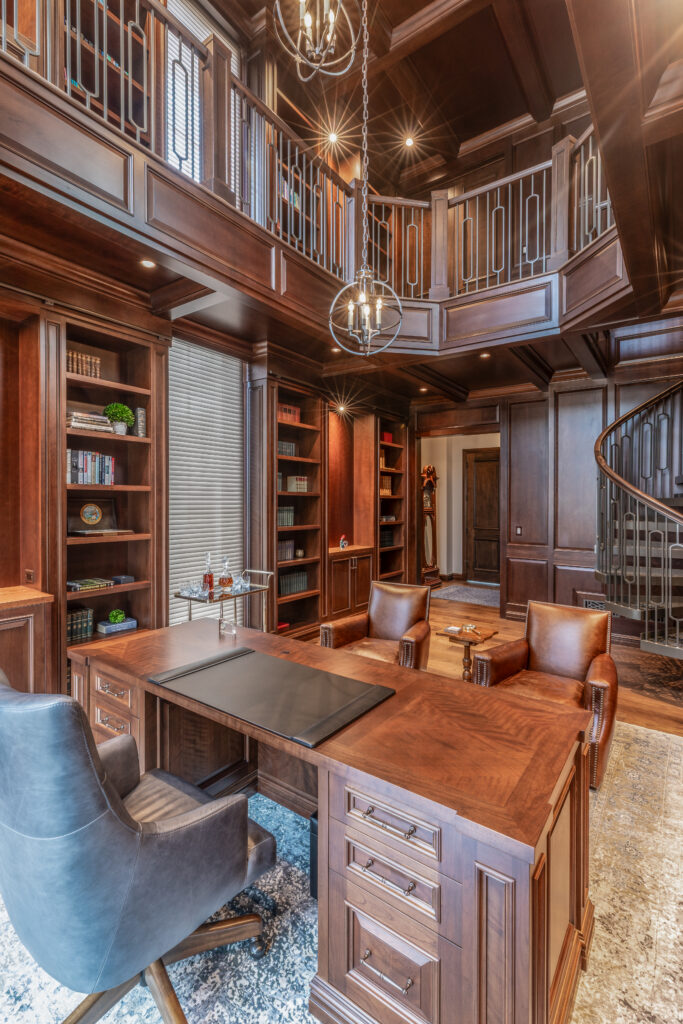 Two story home library in dark wood with a desk and leather chairs.