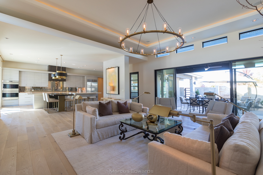 A bright and spacious living room with white sofas and chairs, a chandelier, and floor to ceiling windows.