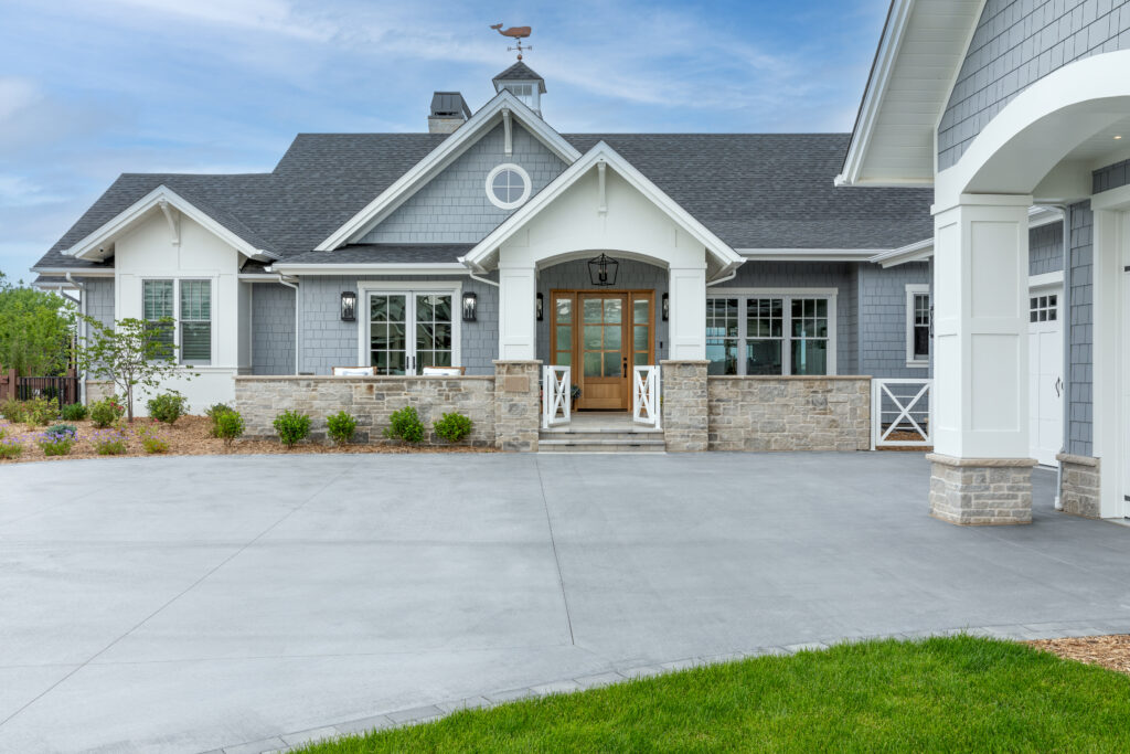 The outside of a white and blue house with a light wood front door and a large driveway.