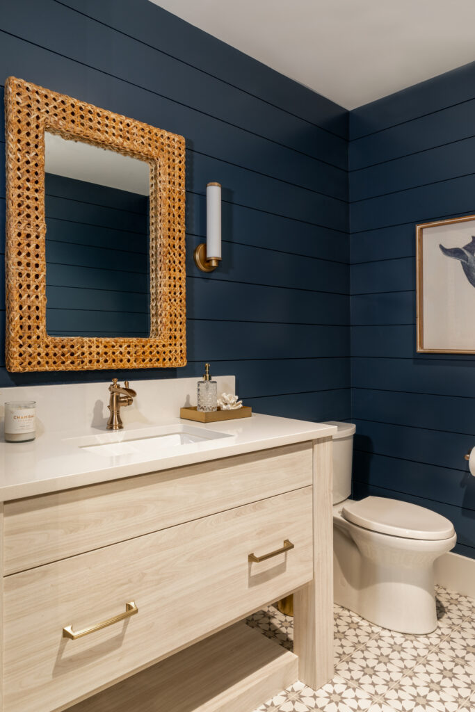 A bathroom with dark blue walls, standalone vanity, tile floor, and a wood framed mirror.