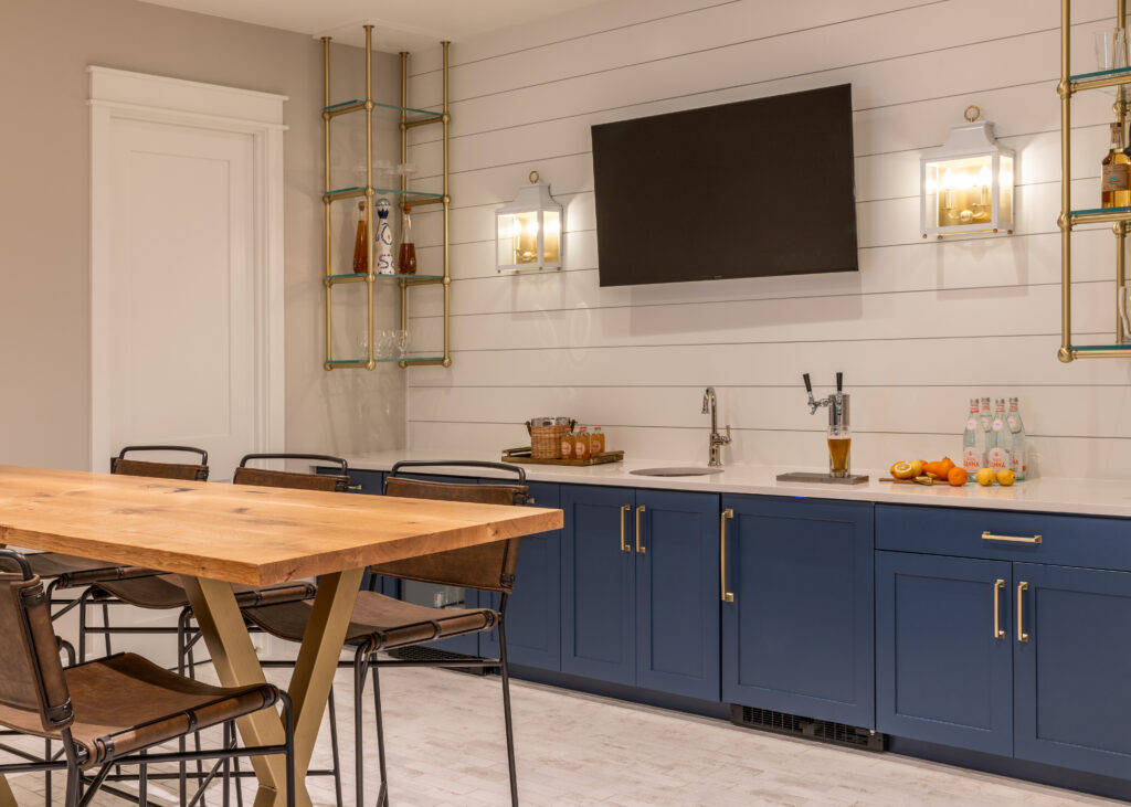A basement kitchen sink with a tv hanging above and a small wooden table on the side.